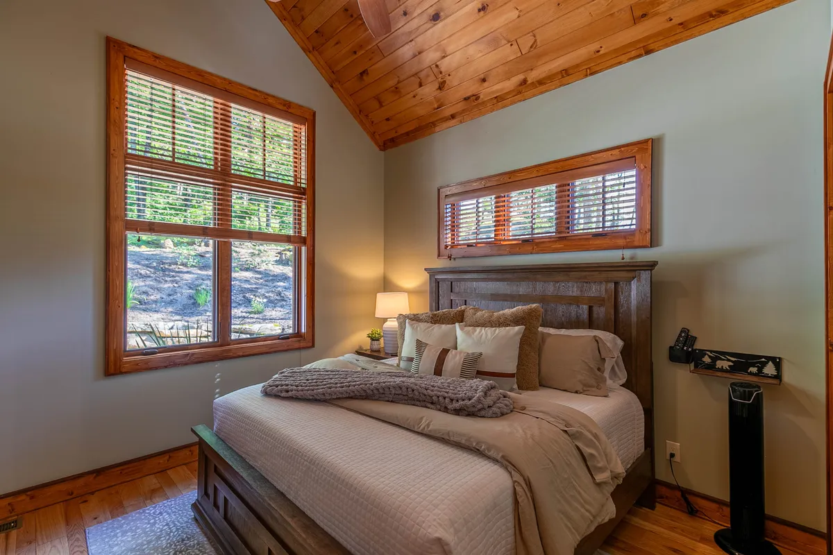 A serene bedroom featuring a comfortable bed with decorative pillows, windows allowing in soft natural light, and a cozy reading lamp. The tranquil setting highlights moments of relaxation and restful escape.