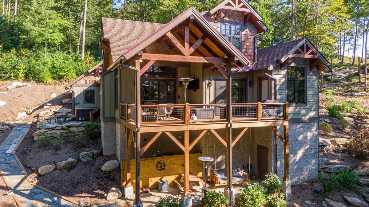 The photo presents a large wooden deck with an intricate roof design, surrounded by vibrant greenery. Visible outdoor furniture suggests a comfortable space for dining or lounging, with sweeping views of the natural landscape creating a sense of tranquility and openness.