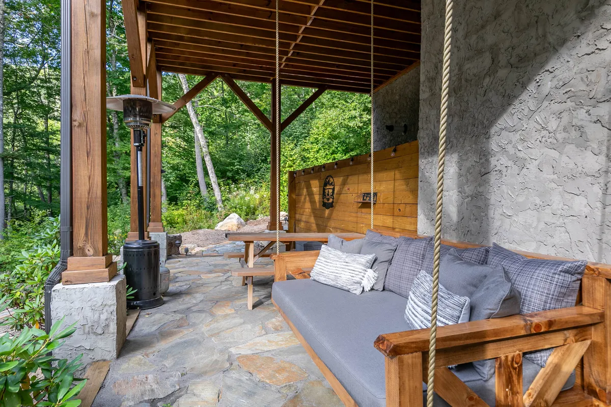 A cozy outdoor lounge area with a swing sofa, wooden beams, stone flooring, and an outdoor heater. The space invites relaxation and socializing while enjoying the surrounding natural landscape, perfect for stargazing or morning coffee.