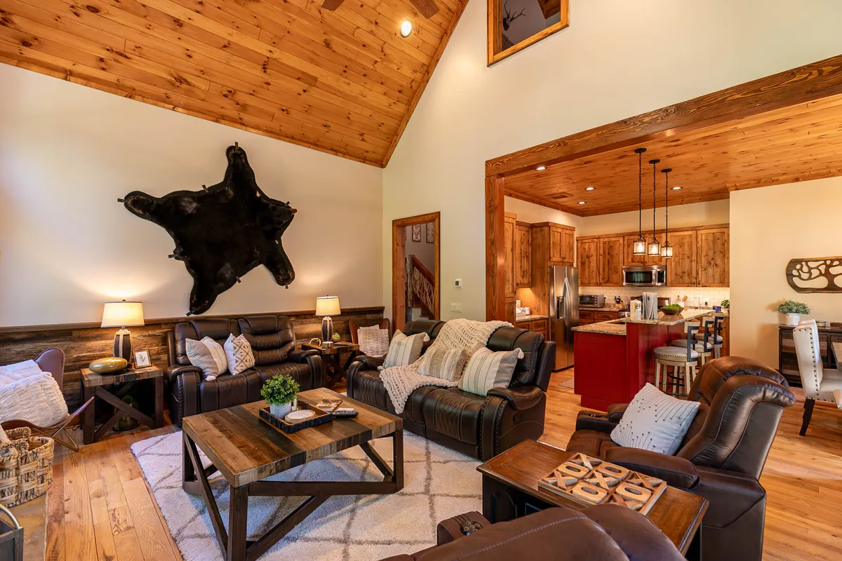 A comfortable living area featuring leather recliners arranged around a wooden coffee table, with cowhide wall art and large windows that flood the space with natural light. The room is perfectly set up for groups to socialize, play games, or unwind after a day of exploration.