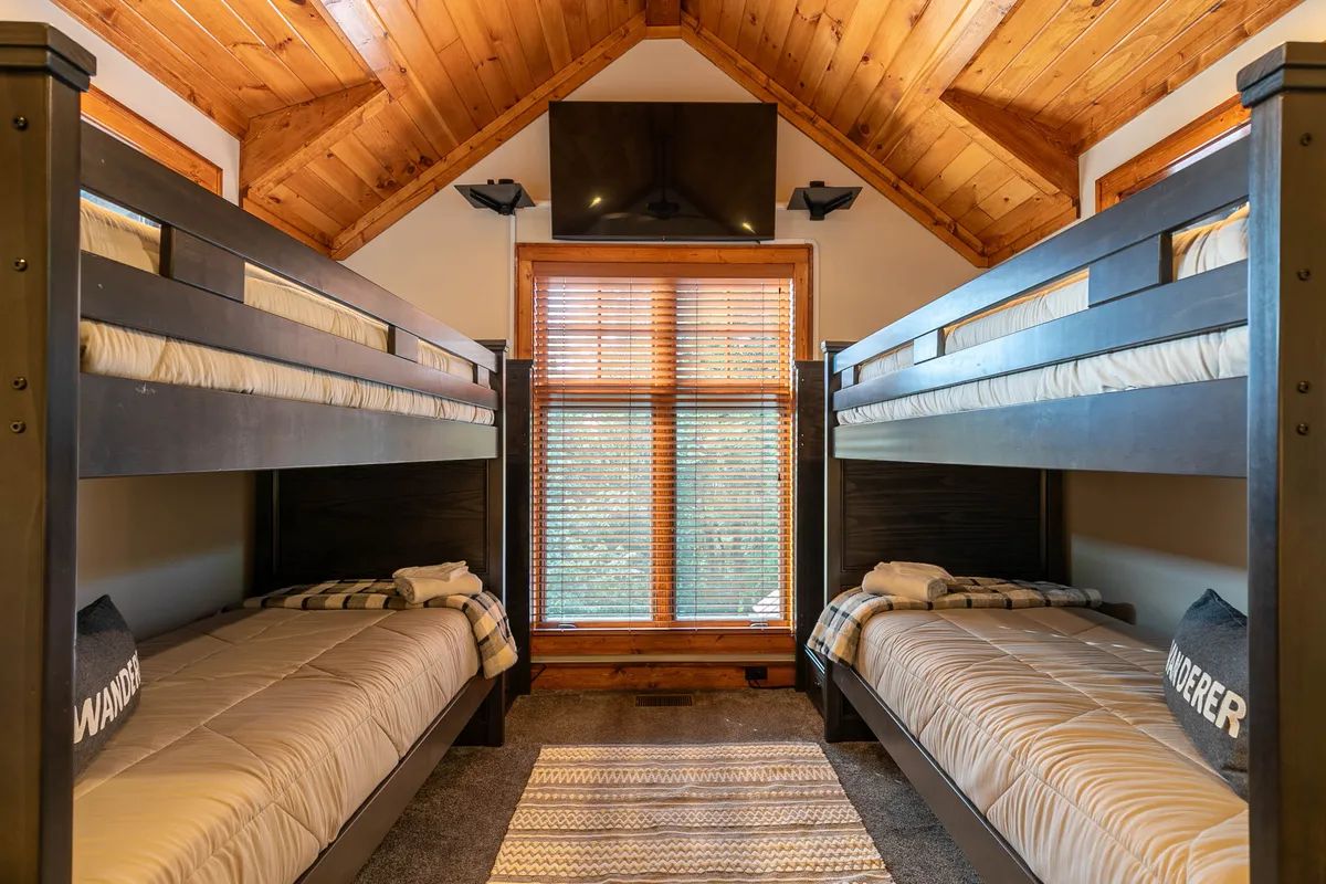 This playful interior image spotlights a bunkroom with multiple beds, a window for natural light, and a cozy rug. The setup is clearly designed for kids, evoking sleepovers, bedtime stories, and fun family vacations.