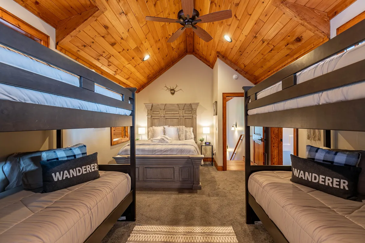 An inviting bunkroom with a main bed and two sets of bunk beds, a wooden ceiling, and playful decorative antlers. The atmosphere is adventurous and welcoming, ideal for families or groups of children to enjoy cozy nights and storytelling.