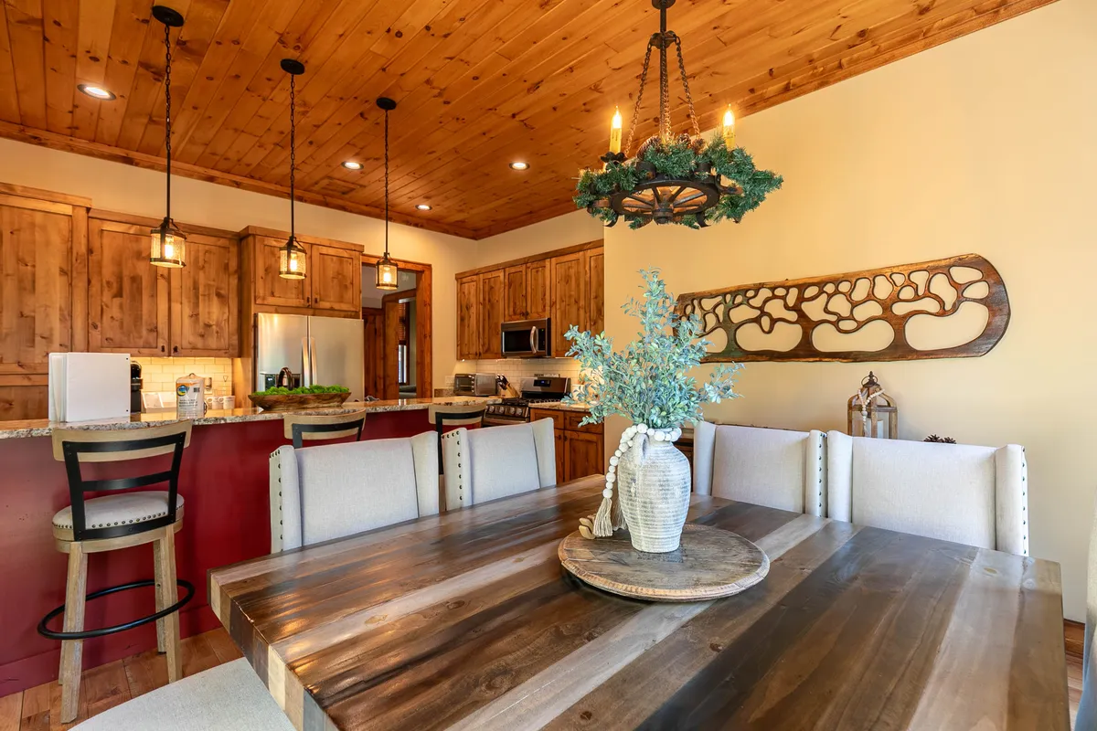 A spacious dining area with a large wooden table, elegant chandelier, and decorative wall art, framed by warm lighting and wood cabinetry. The setting is ideal for group meals, celebrations, and connecting over shared experiences.