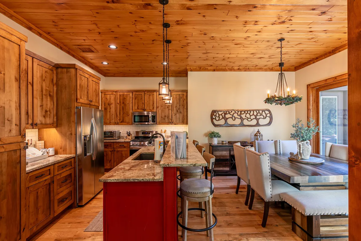 A cozy kitchen and dining zone featuring a prominent granite countertop, warm wooden cabinetry, a large dining table with chairs, decorative wall art, and stylish hanging lights. The setup is ideal for family meals or festive gatherings.